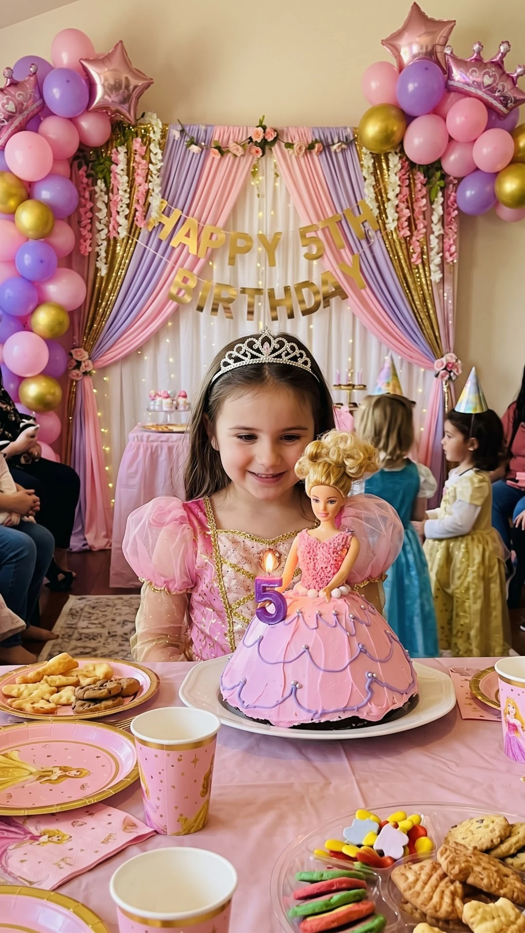 Pink princess birthday cake inspiration with a doll-shaped cake, number five candle, a child wearing a tiara and pink-and-lilac decorations