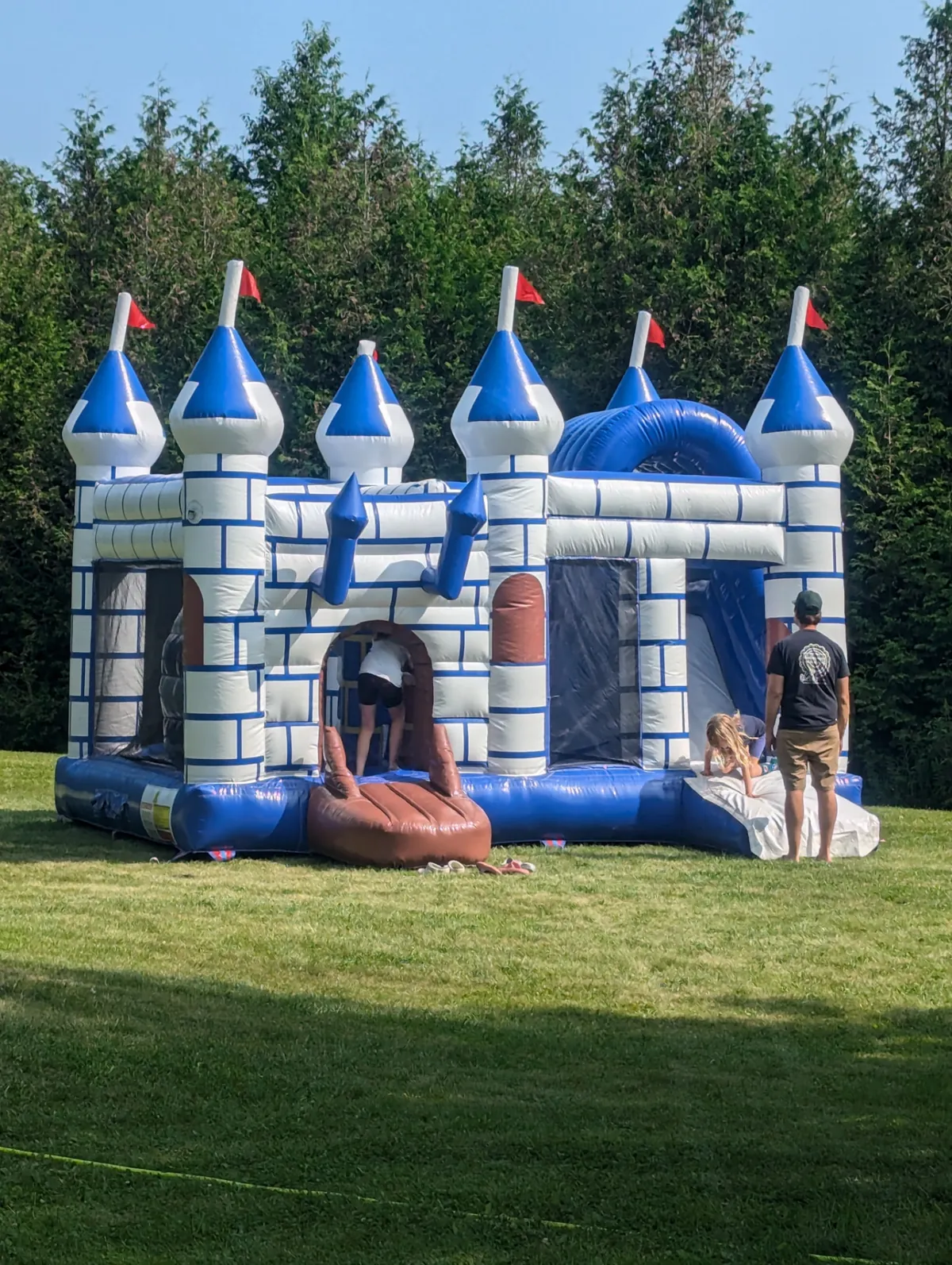 Blue and white Castle Royal inflatable bouncy castle with kids playing inside on a backyard lawn